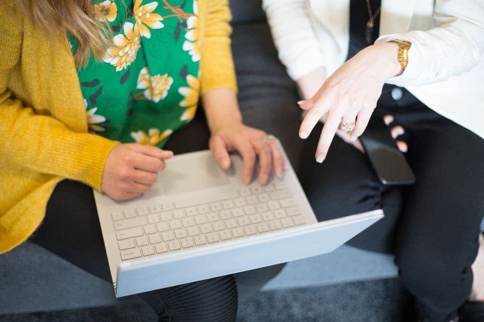 Dos personas sentadas una junto a la otra revisan juntas un portátil; se ven sus manos y el teclado.